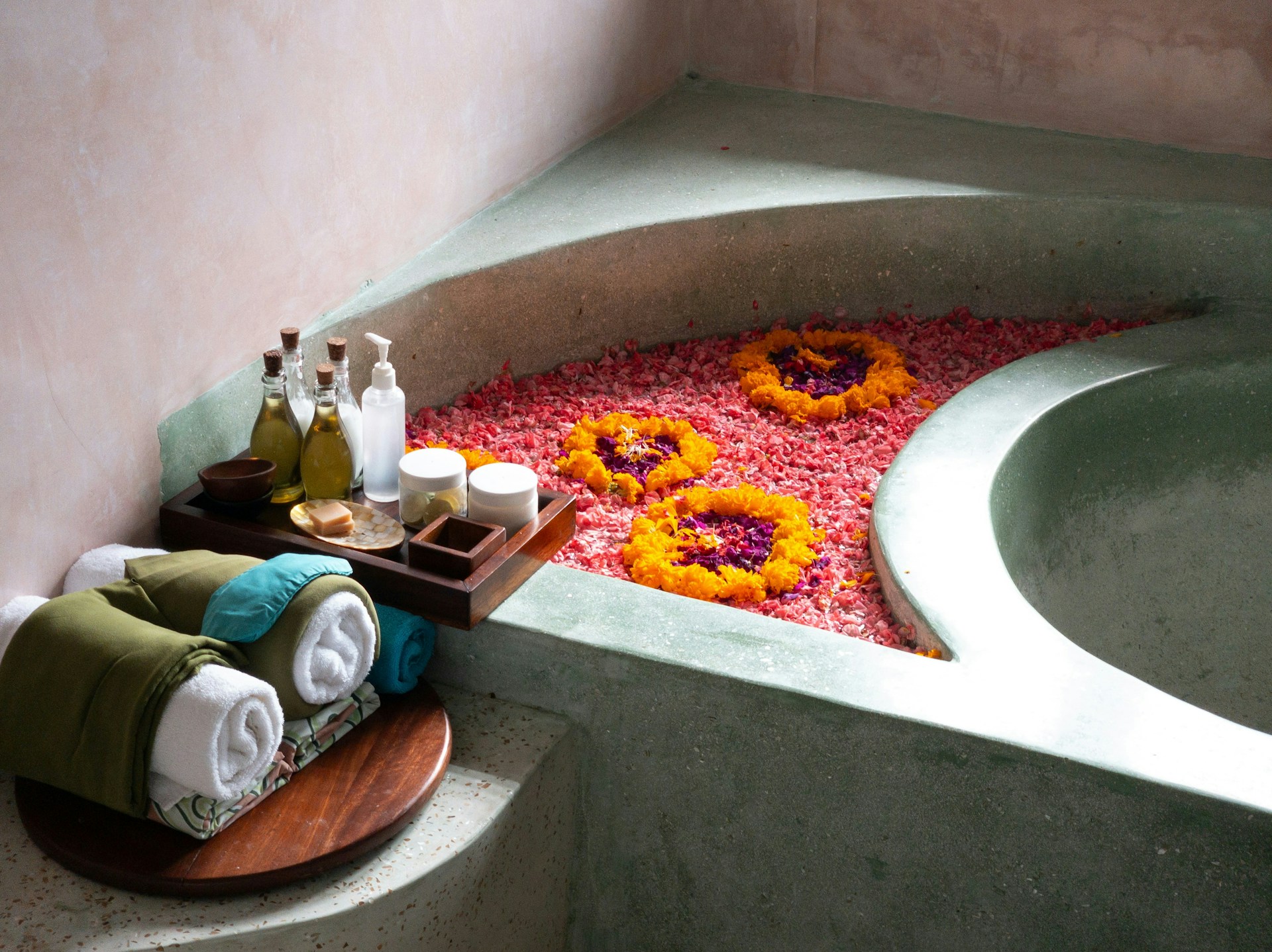 Stone spa bath filled with flower petals beside towels and massage oils